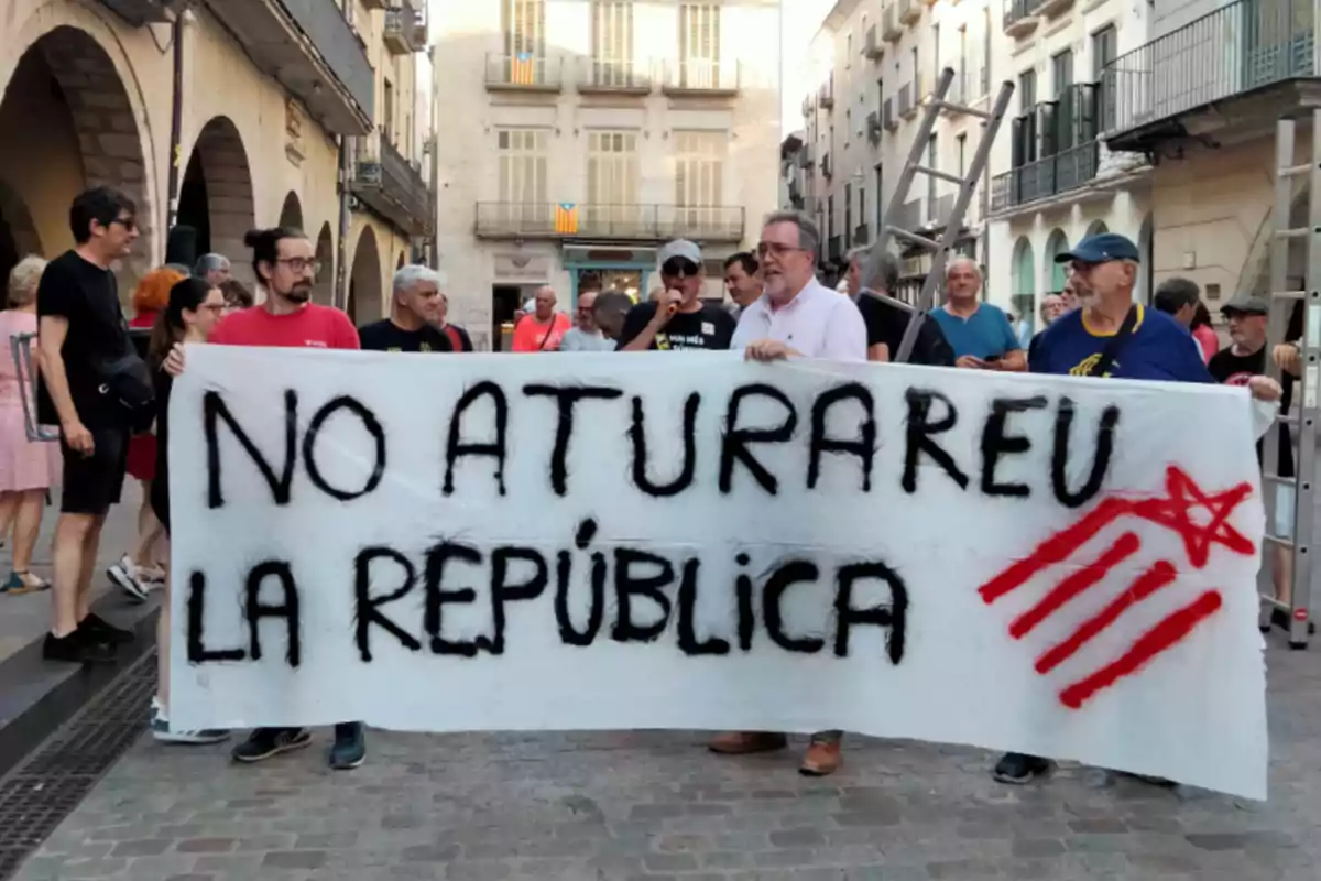 Un grup de persones sosté una pancarta blanca amb el missatge No aturareu la república escrit en lletres negres i un símbol vermell en un carrer d’una ciutat.