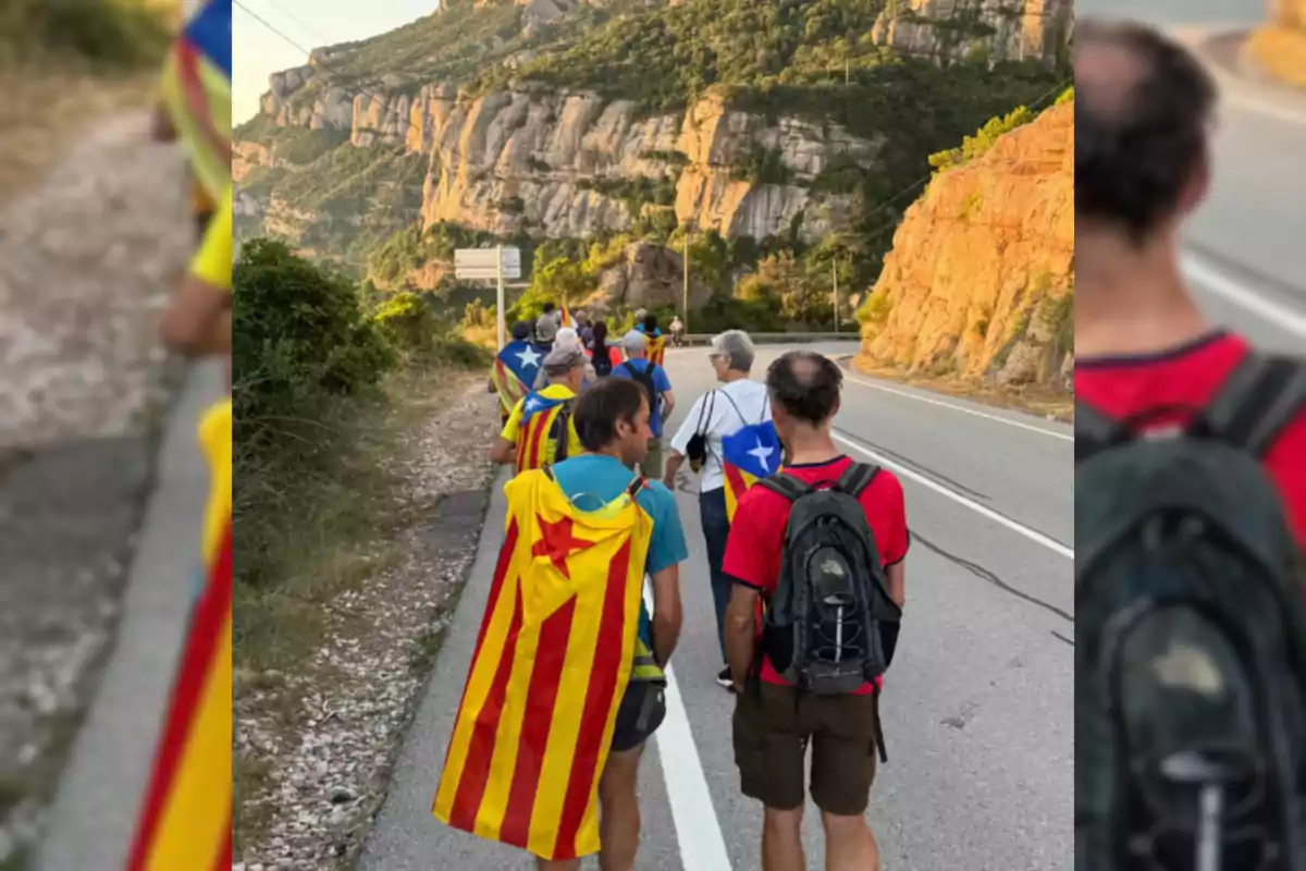 Grup de persones caminant per una carretera de muntanya, algunes porten banderes estelades sobre les espatlles