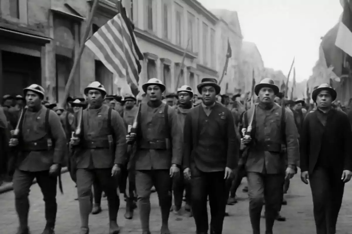 Soldats afroamericans desfilen en formació per un carrer durant la Primera Guerra Mundial portant banderes i uniformes històrics. Soldats afroamericans desfilen en formació per un carrer durant la Primera Guerra Mundial portant banderes i uniformes històrics.