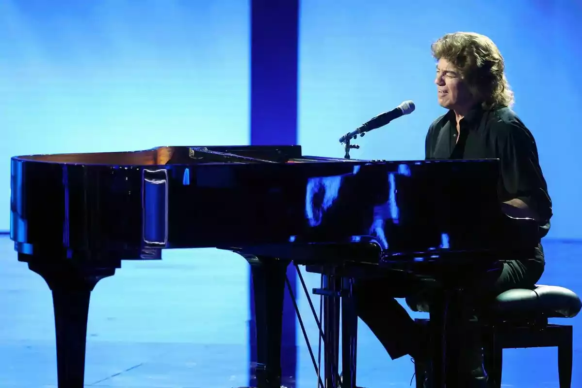 Bertín Osborne tocant el piano de cua i cantant en un escenari il·luminat amb llum blava de Tu Cara Me Suena Bertín Osborne tocant el piano de cua i cantant en un escenari il·luminat amb llum blava de Tu Cara Me Suena