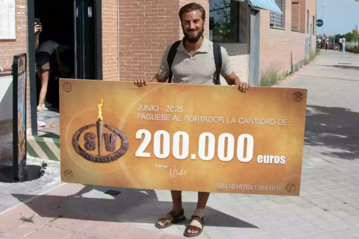 Borja González somrient sosté un xec gegant de 200.000 euros al carrer davant d’un edifici de maó. Borja González somrient sosté un xec gegant de 200.000 euros al carrer davant d’un edifici de maó.