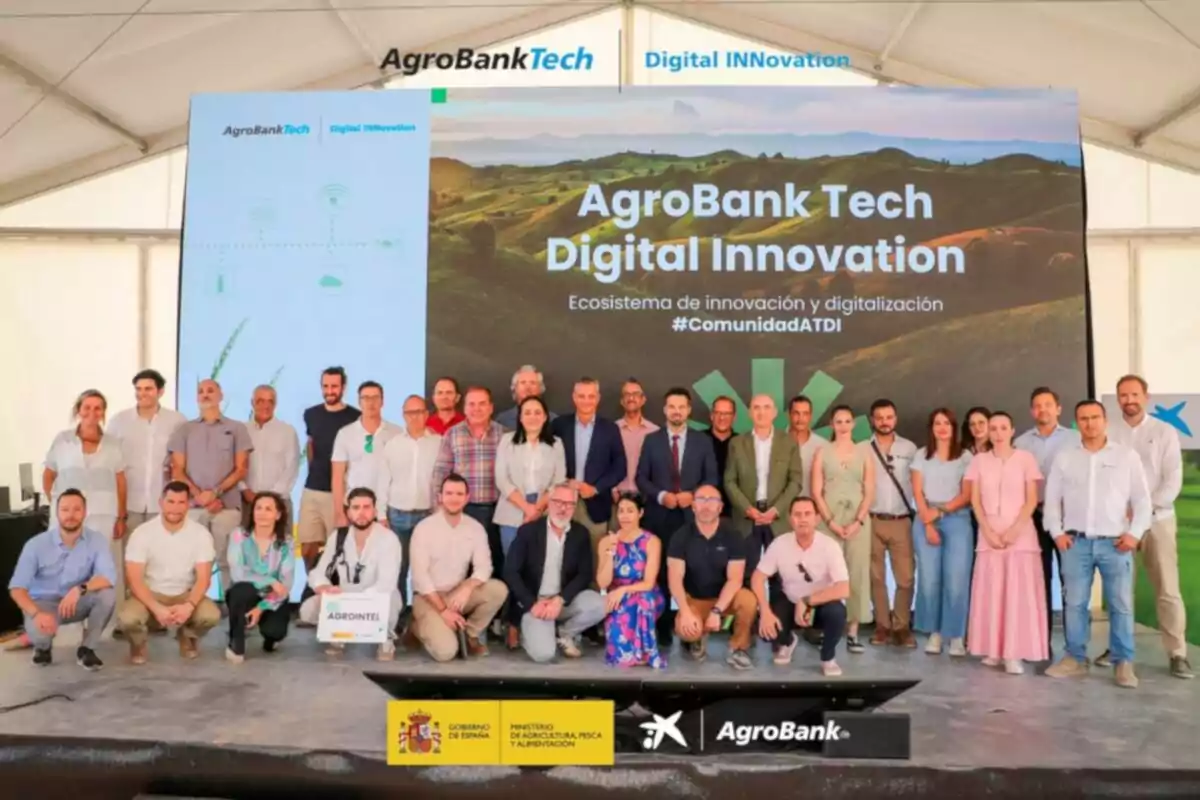 Grup de persones posant davant d’un escenari amb un cartell d’AgroBank Tech Digital Innovation en un esdeveniment sobre innovació i digitalització en el sector agrícola Grup de persones posant davant d’un escenari amb un cartell d’AgroBank Tech Digital Innovation en un esdeveniment sobre innovació i digitalització en el sector agrícola