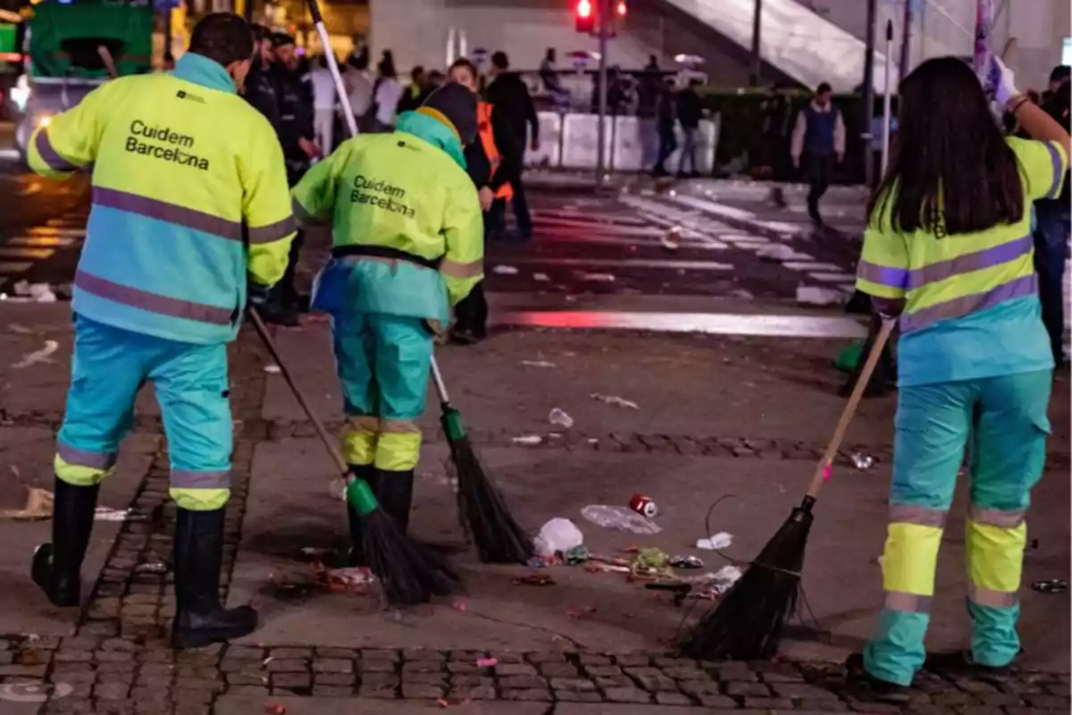 Treballadors de neteja amb uniformes reflectants escombren escombraries en un carrer durant la nit a Barcelona. Treballadors de neteja amb uniformes reflectants escombren escombraries en un carrer durant la nit a Barcelona.