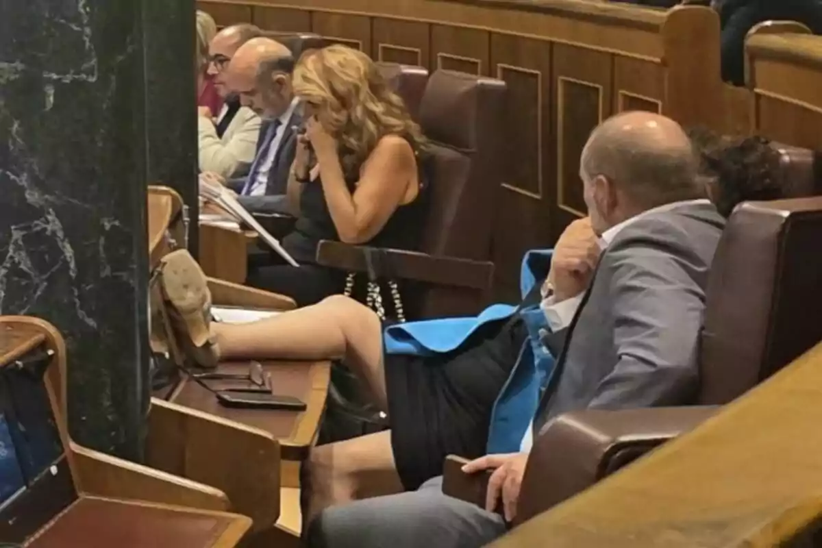 Una persona asseguda en una sala de reunions amb la cama estesa sobre l'escriptori mentre altres persones estan concentrades en els seus documents. Una persona asseguda en una sala de reunions amb la cama estesa sobre l'escriptori mentre altres persones estan concentrades en els seus documents.