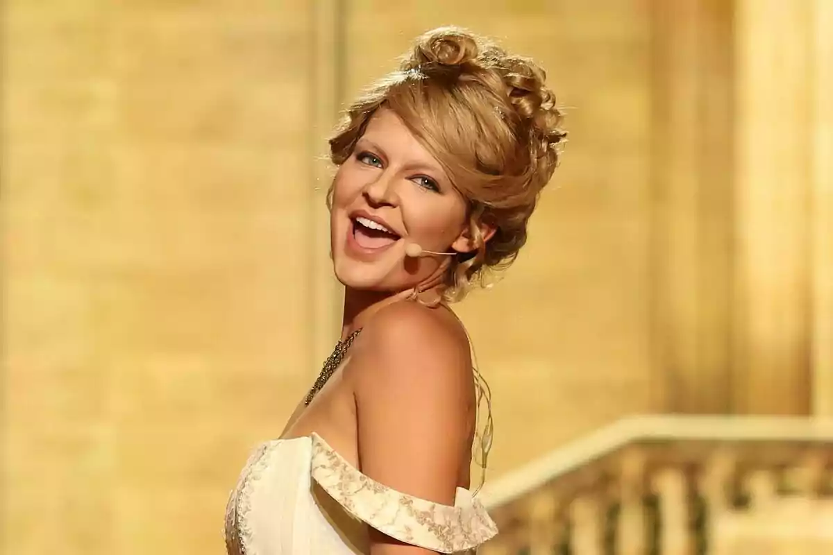 Laura Escanes amb vestit elegant i micròfon de diadema somrient en un escenari il·luminat a Tu Cara Me Suena