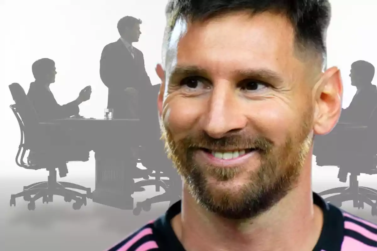 Close-up of a smiling man with a beard and a sports jersey, with silhouettes of people in an office meeting in the background.