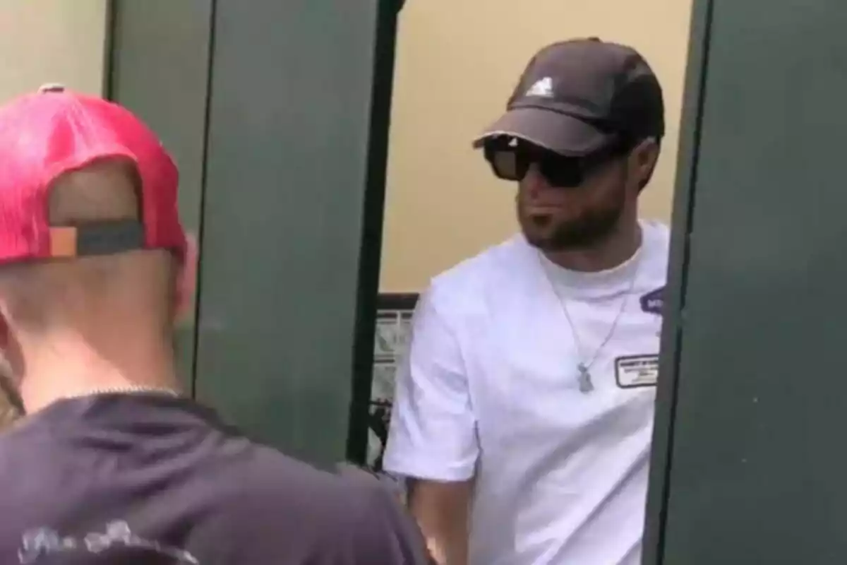 Montoya amb gorra, ulleres de sol i samarreta informal és a prop d’una porta verda.