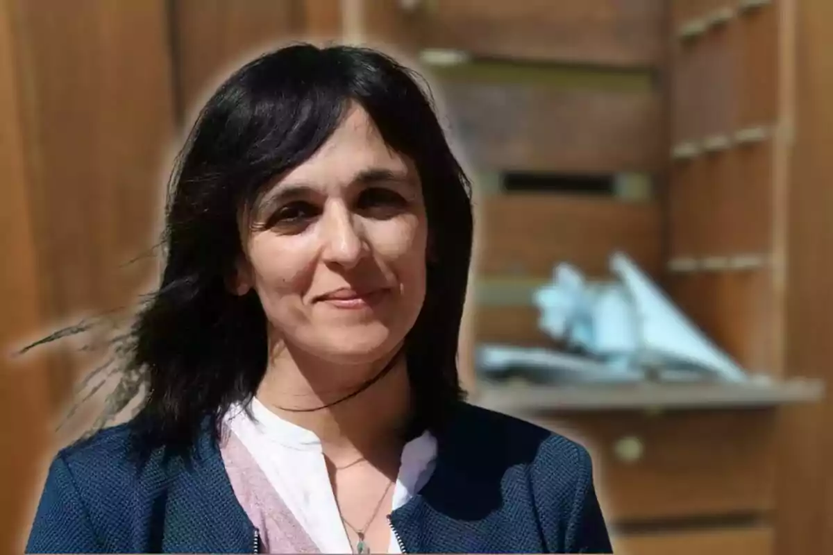 Dark-haired, straight-haired woman slightly smiling in front of a blurred wooden background