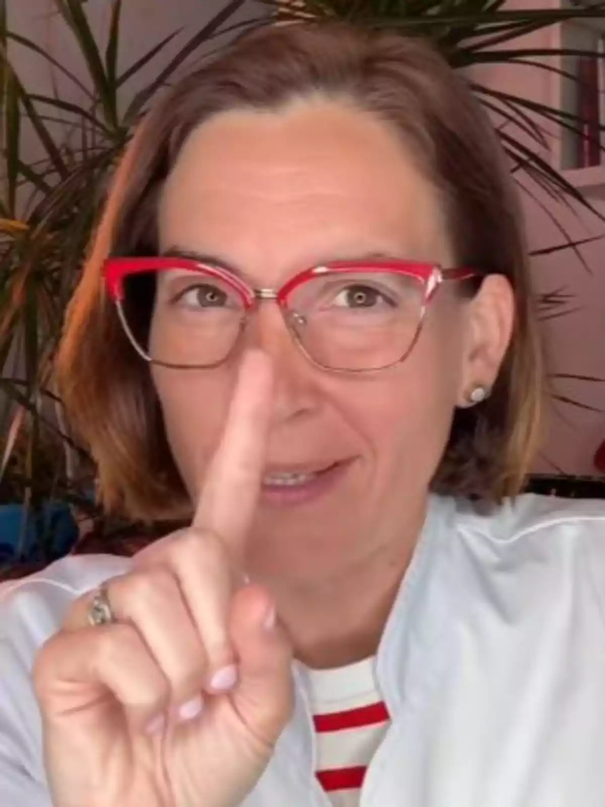 Dona amb ulleres vermelles assenyalant cap amunt amb el dit índex i somrient Dona amb ulleres vermelles assenyalant cap amunt amb el dit índex i somrient