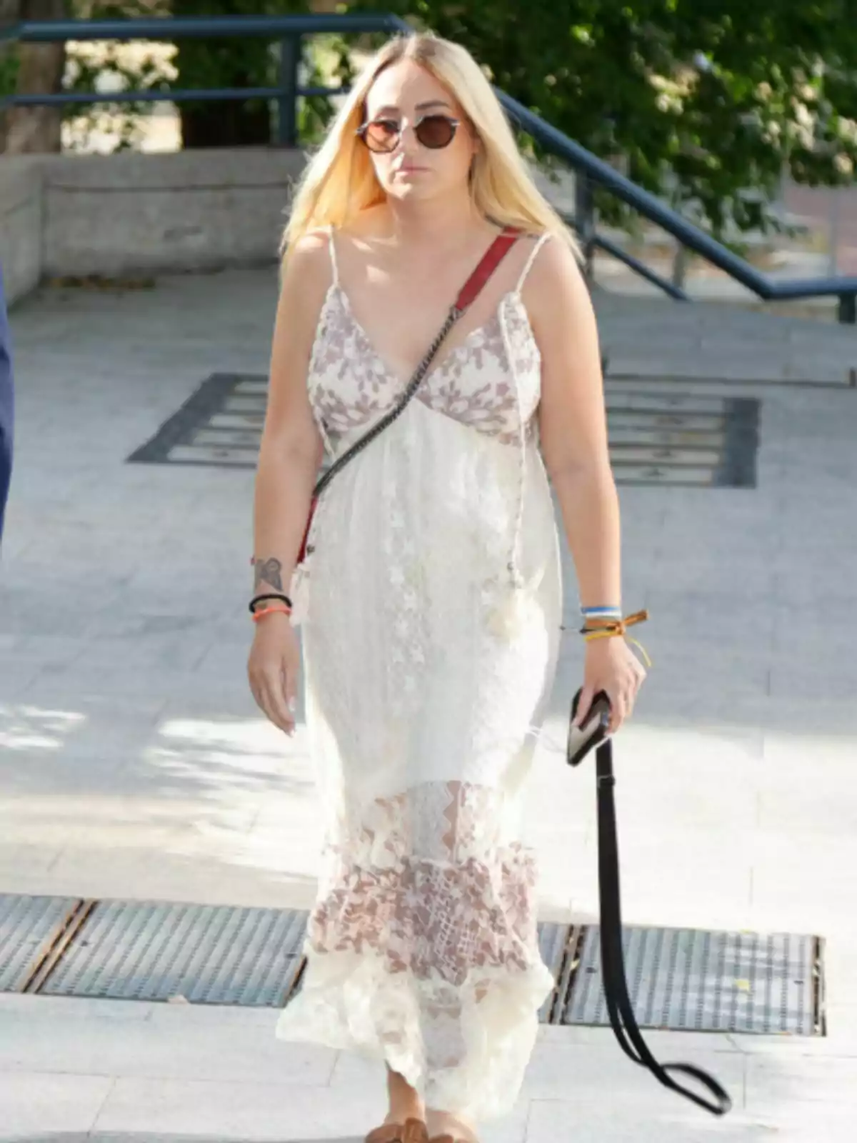 Rocío Flores wearing sunglasses and a long white dress with brown details walking down the street Rocío Flores wearing sunglasses and a long white dress with brown details walking down the street