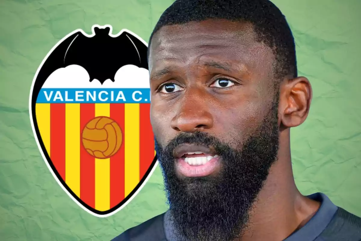 Un home amb barba en primer pla i l’escut del València Club de Futbol al fons sobre un fons verd.