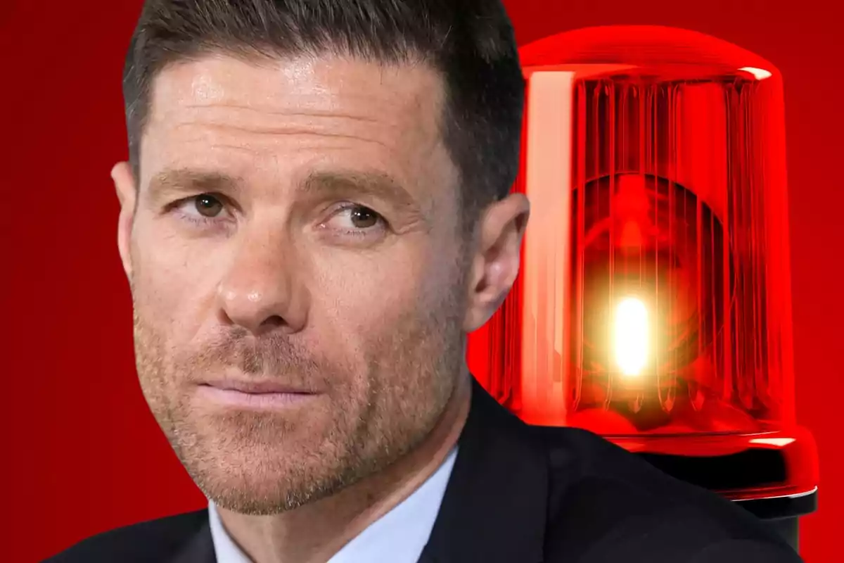 Short-haired, bearded man with a serious expression in front of a lit red emergency siren against a red background