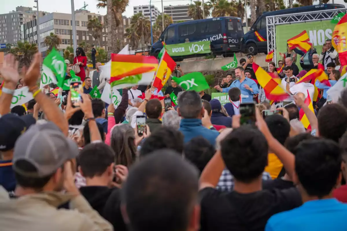 Multitud de persones en un míting polític a l’aire lliure amb banderes d’Espanya i pancartes verdes de Vox mentre un orador s’adreça al públic i diverses persones graven l’escena amb els seus telèfons mòbils.