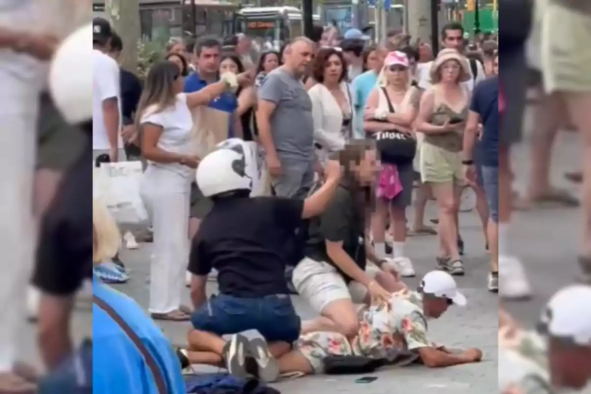 Una multitud observa mientras dos personas inmovilizan a un hombre en el suelo en una calle concurrida