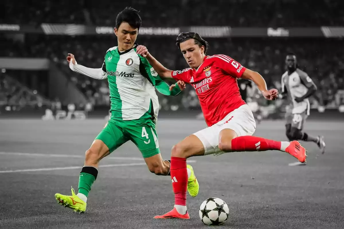 Dos futbolistes disputen la pilota durant un partit en un estadi ple d’espectadors Dos futbolistes disputen la pilota durant un partit en un estadi ple d’espectadors