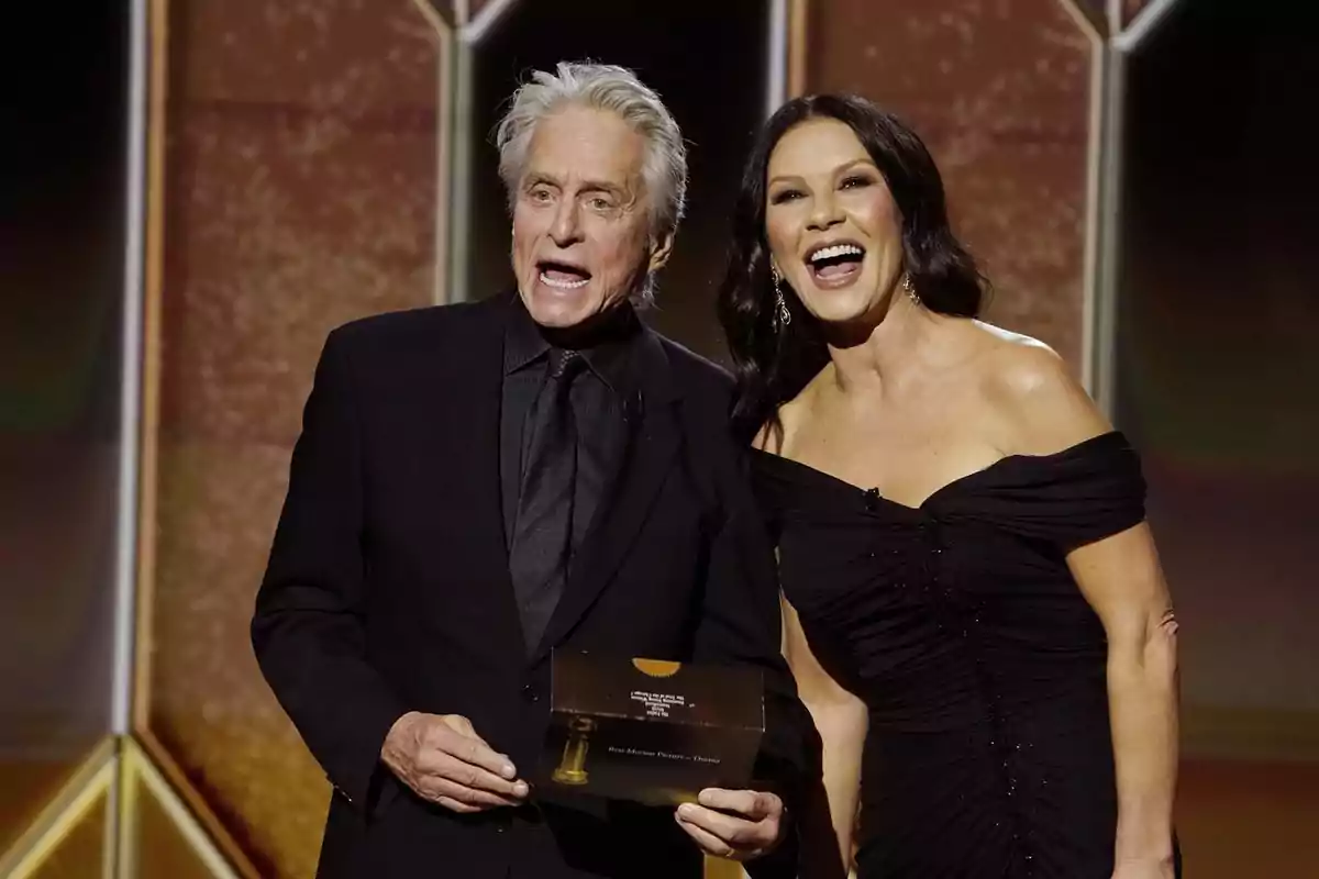 Catherine Zeta-Jones and Michael Douglas, elegantly dressed, smile as they present an award on a brightly lit stage. Catherine Zeta-Jones and Michael Douglas, elegantly dressed, smile as they present an award on a brightly lit stage.