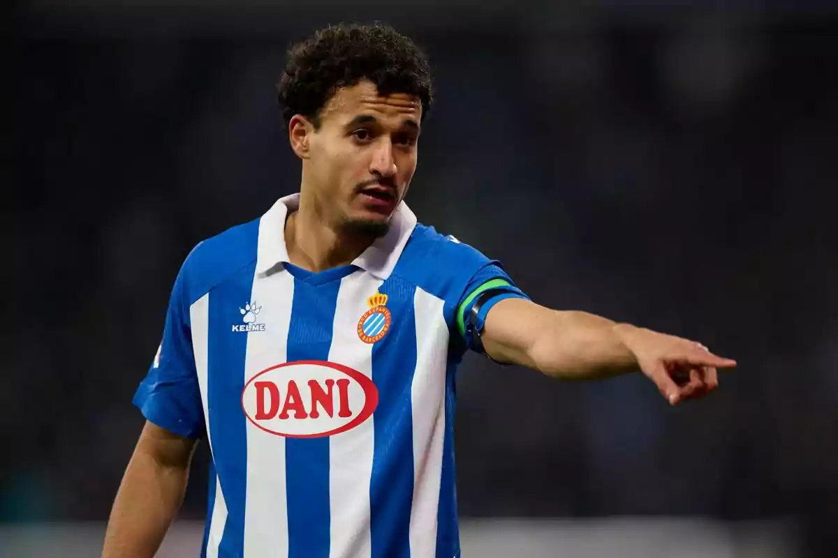 Futbolista amb uniforme blau i blanc de l’Espanyol assenyalant amb el braç estès durant un partit