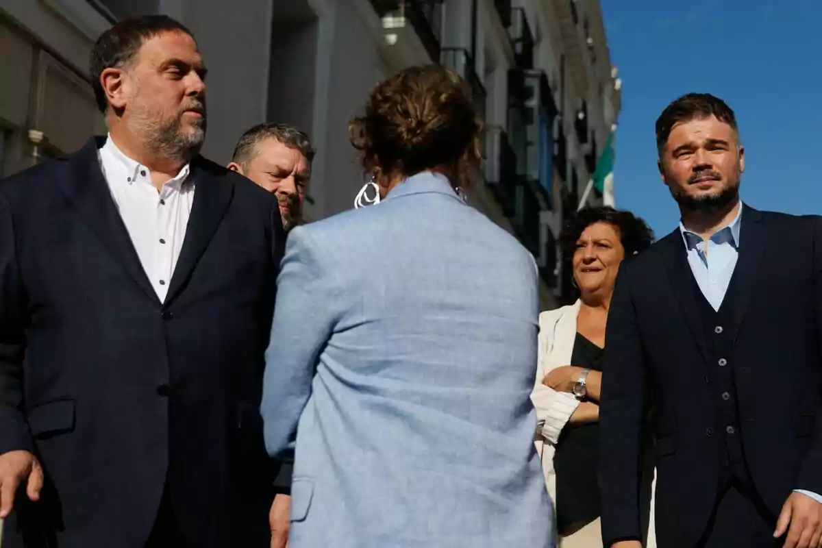 Five people dressed formally are talking outdoors on a street with buildings and a clear sky. Five people dressed formally are talking outdoors on a street with buildings and a clear sky.
