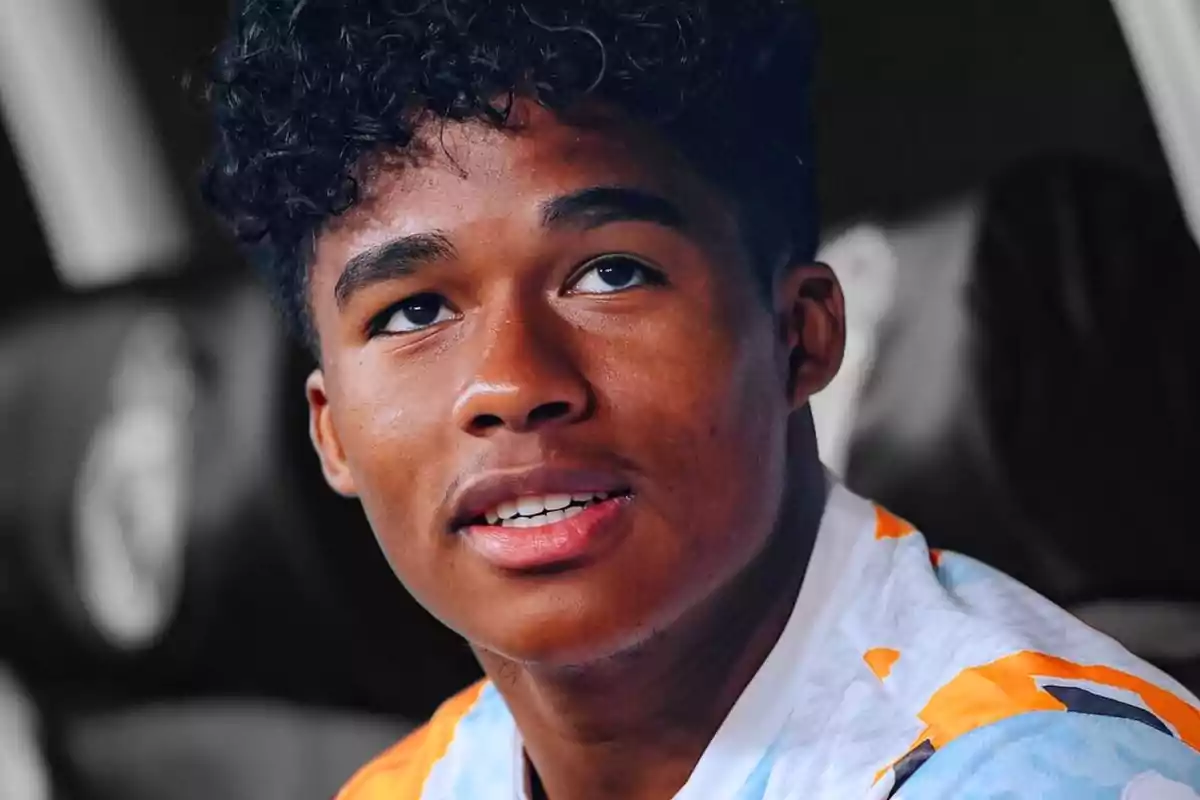 Young man with curly hair and a sports jersey looking up with a thoughtful expression