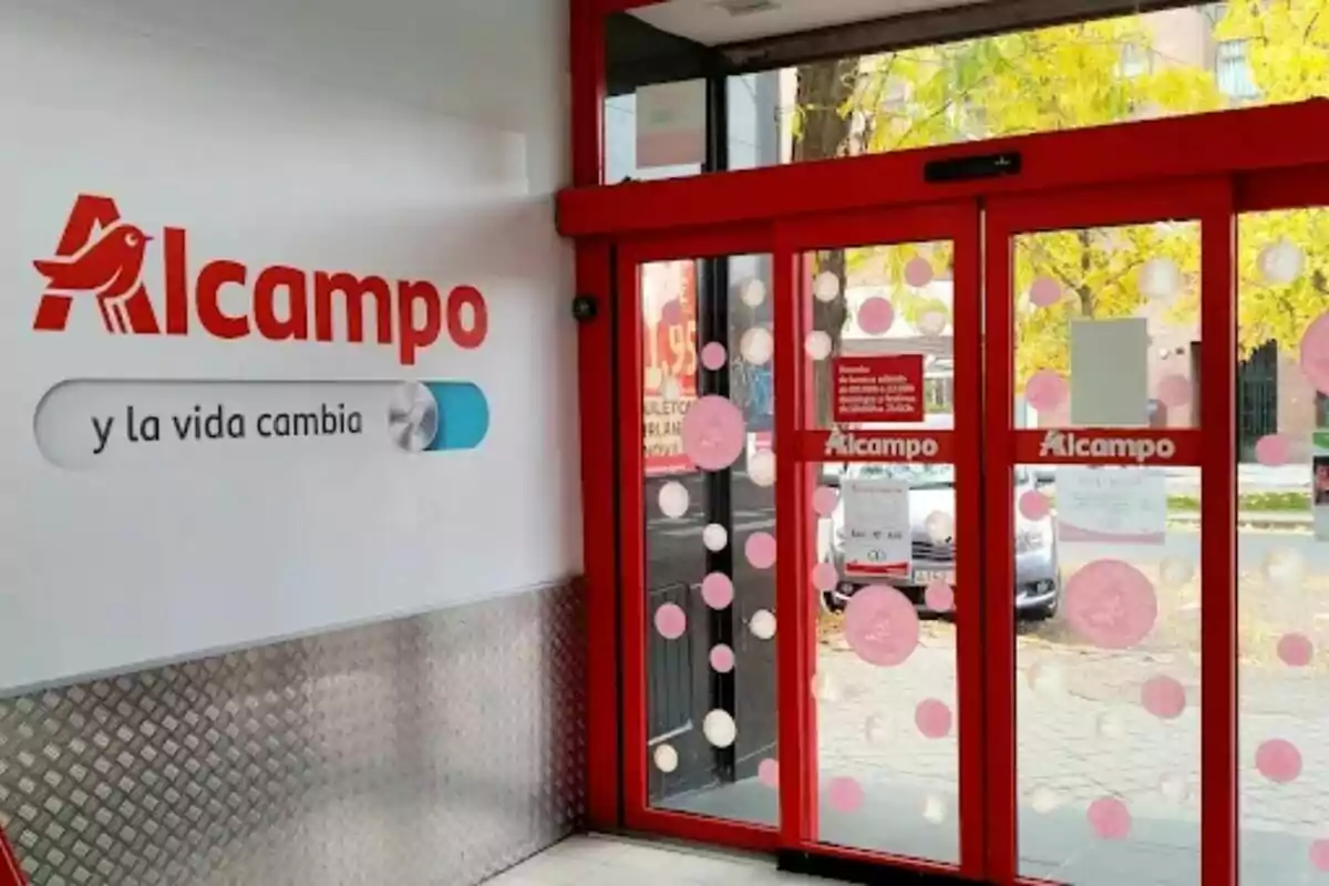 Alcampo supermarket entrance with automatic glass doors decorated with circles and the logo visible on the wall and on the doors. Alcampo supermarket entrance with automatic glass doors decorated with circles and the logo visible on the wall and on the doors.