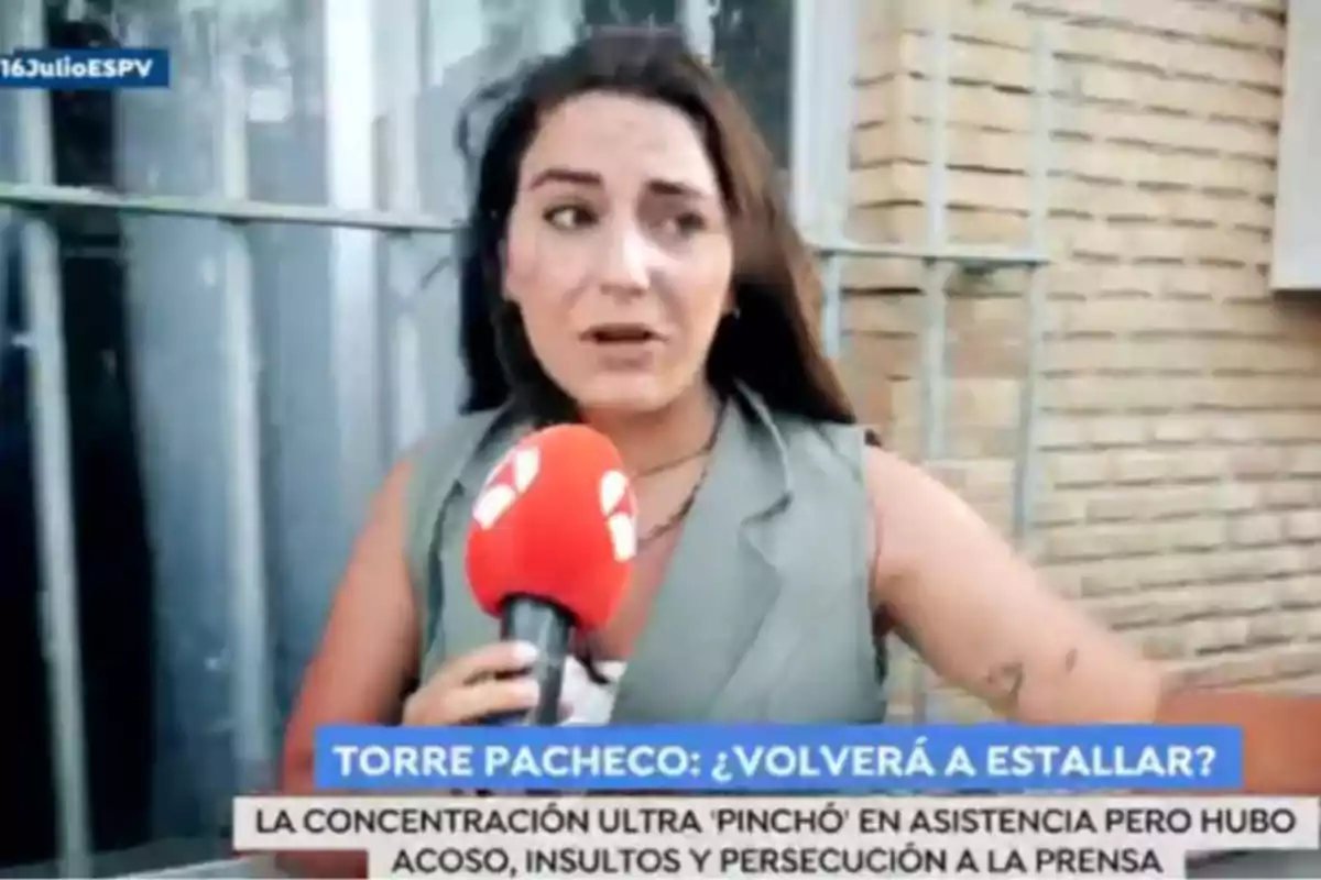 Reporter with a red microphone reporting on the street in front of a brick wall, with a news ticker at the bottom of the image. Screenshot from 'Espejo Público' Reporter with a red microphone reporting on the street in front of a brick wall, with a news ticker at the bottom of the image. Screenshot from 'Espejo Público'