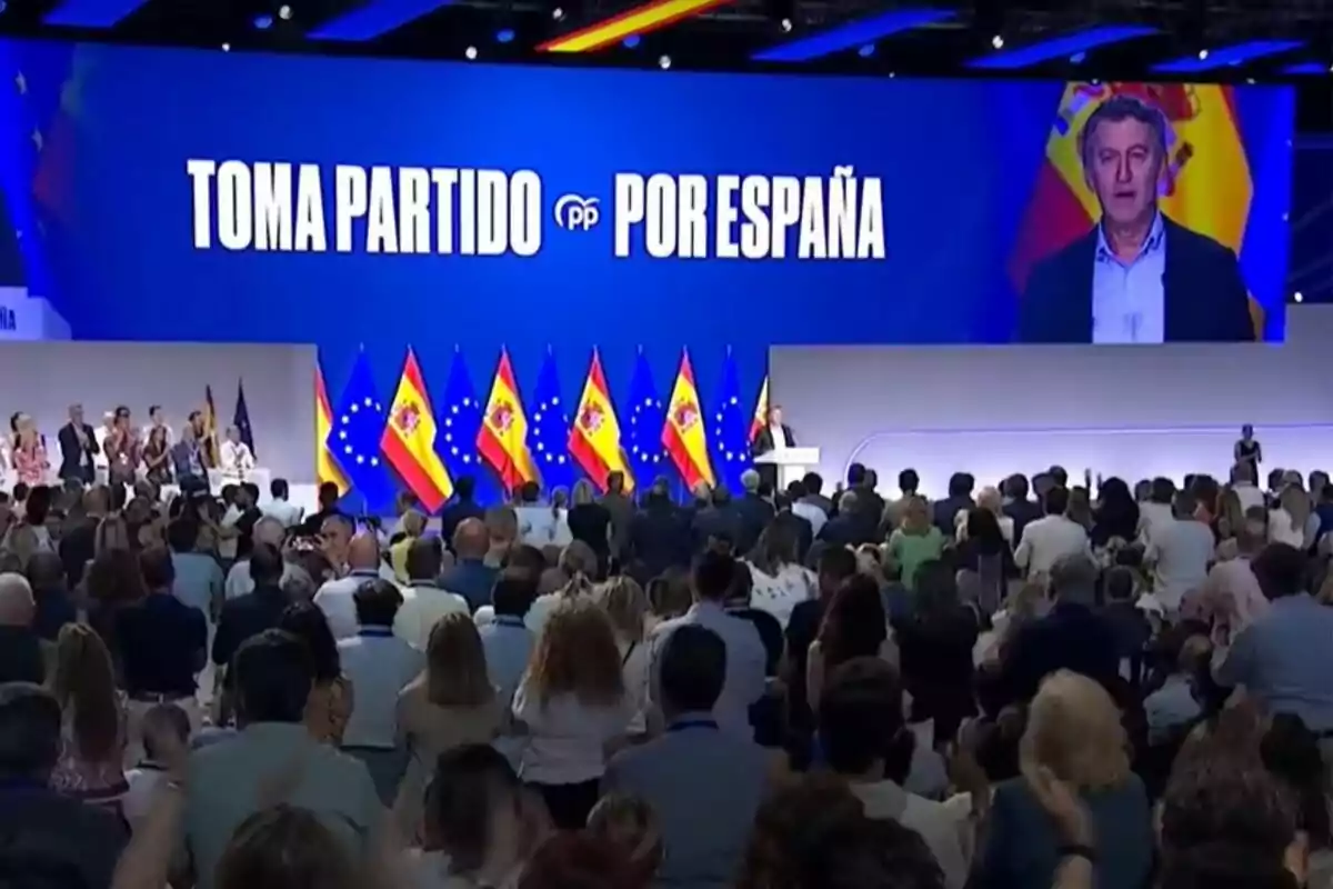 Auditorium full of people attending a political event of the People's Party in Spain, with Spanish and European flags on the stage and a large screen displaying the message Auditorium full of people attending a political event of the People's Party in Spain, with Spanish and European flags on the stage and a large screen displaying the message