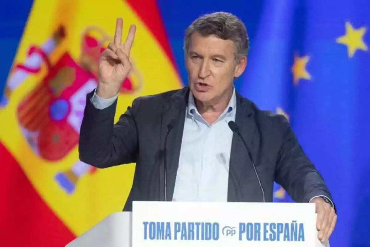 Man speaking at a podium with the text "Take a Stand for Spain," making a hand gesture, with Spanish and European Union flags in the background.
