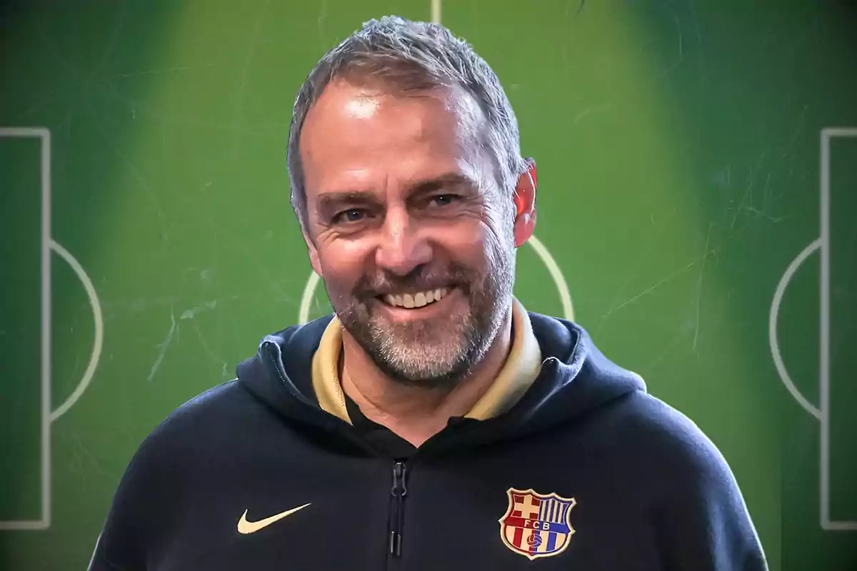 Hombre sonriente con barba y sudadera del FC Barcelona frente a un fondo de cancha de fútbol Hombre sonriente con barba y sudadera del FC Barcelona frente a un fondo de cancha de fútbol