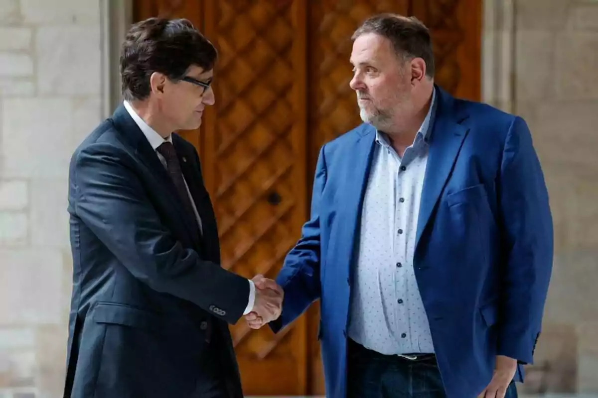 Two men in suits shake hands while looking at each other in a formal setting with a wooden door in the background.