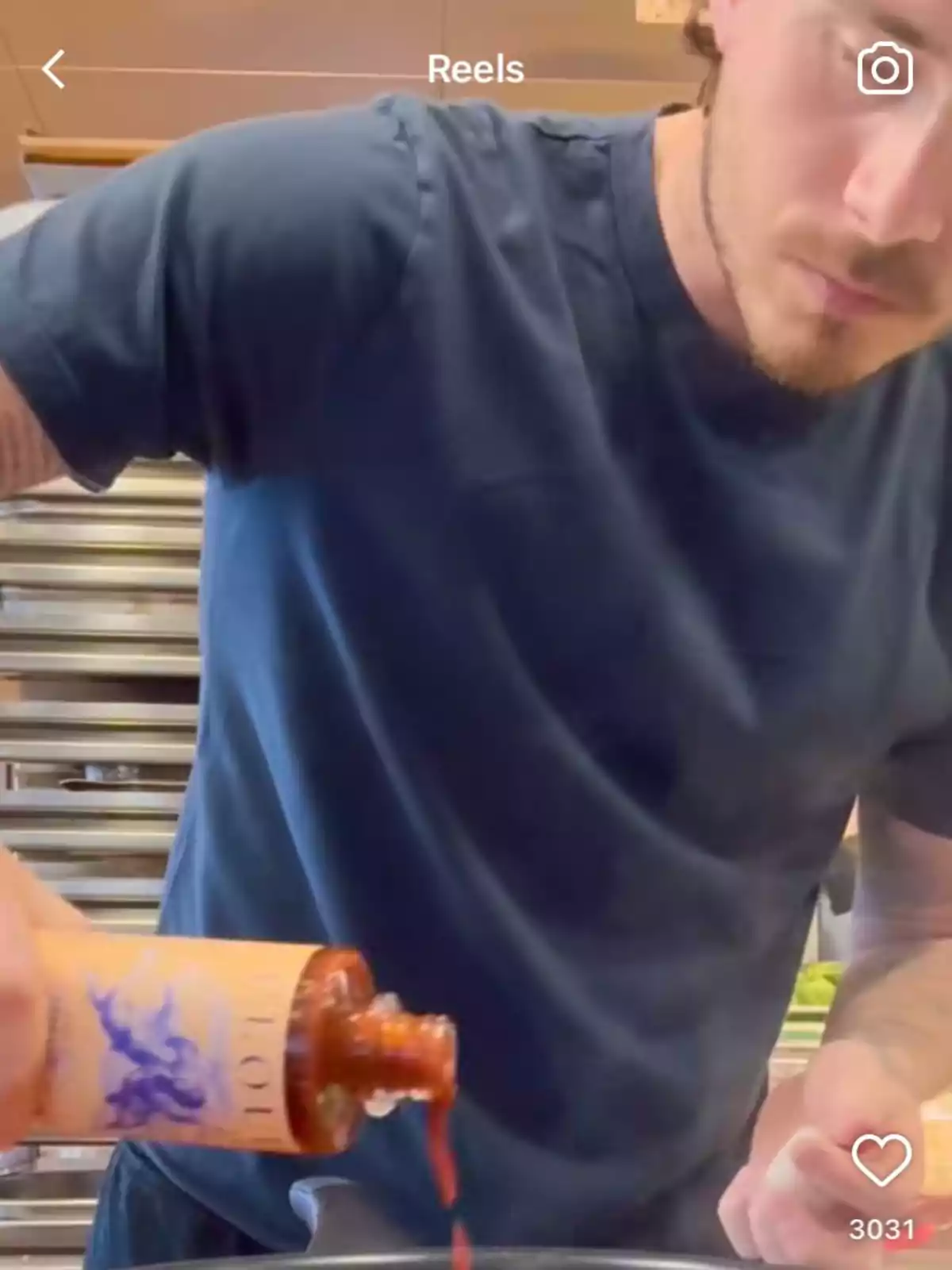 Man in a blue jersey pouring sauce from a bottle onto a plate in a kitchen Man in a blue jersey pouring sauce from a bottle onto a plate in a kitchen