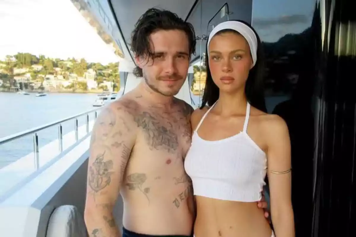 Young couple posing on the deck of a yacht overlooking the sea with houses in the background Young couple posing on the deck of a yacht overlooking the sea with houses in the background