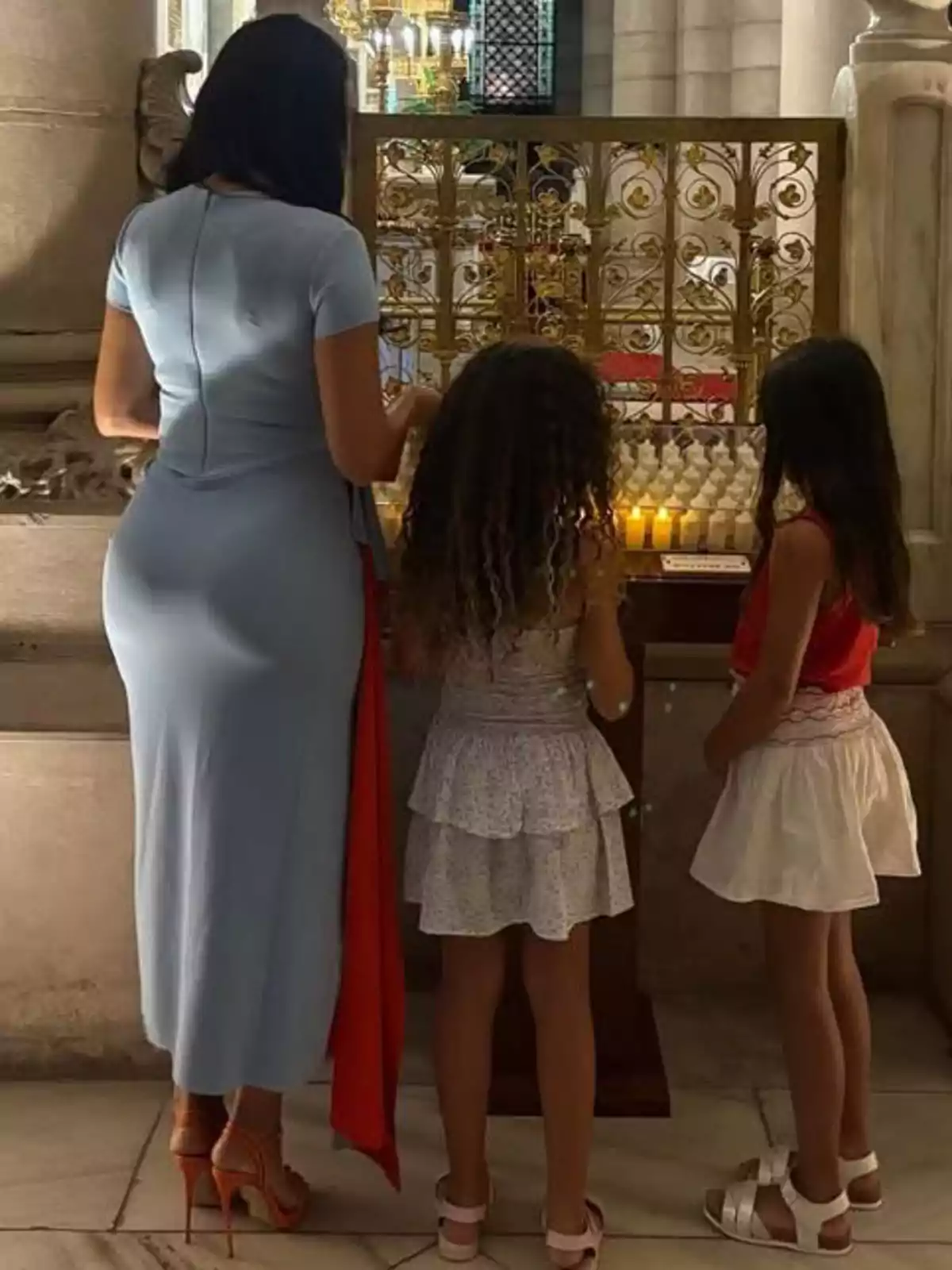 Dona i dues nenes d’esquena encenent espelmes en una església Dona i dues nenes d’esquena encenent espelmes en una església