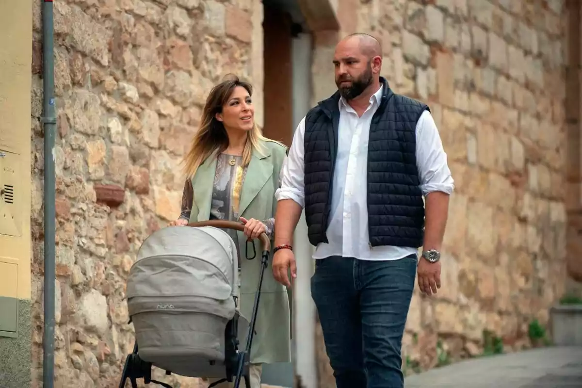 Una parella camina per un carrer empedrat mentre la dona empeny un cotxet de nadó i tots dos conversen relaxadament. Una parella camina per un carrer empedrat mentre la dona empeny un cotxet de nadó i tots dos conversen relaxadament.