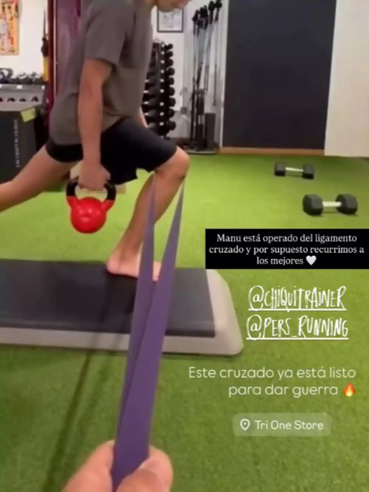 Persona realitzant exercici de gambada amb pesa russa i banda elàstica en un gimnàs sobre gespa artificial Persona realitzant exercici de gambada amb pesa russa i banda elàstica en un gimnàs sobre gespa artificial