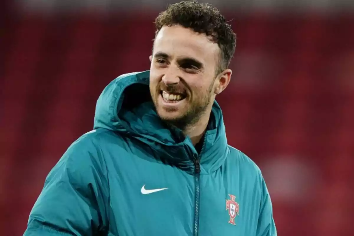 Diogo Jota wearing a sea green sports jacket with the Portugal crest, smiling in a stadium
