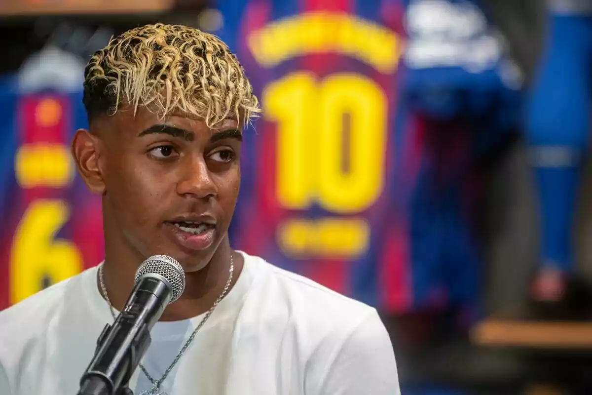 Young man with curly blond hair speaking in front of a microphone with Barcelona soccer jerseys in the background Young man with curly blond hair speaking in front of a microphone with Barcelona soccer jerseys in the background