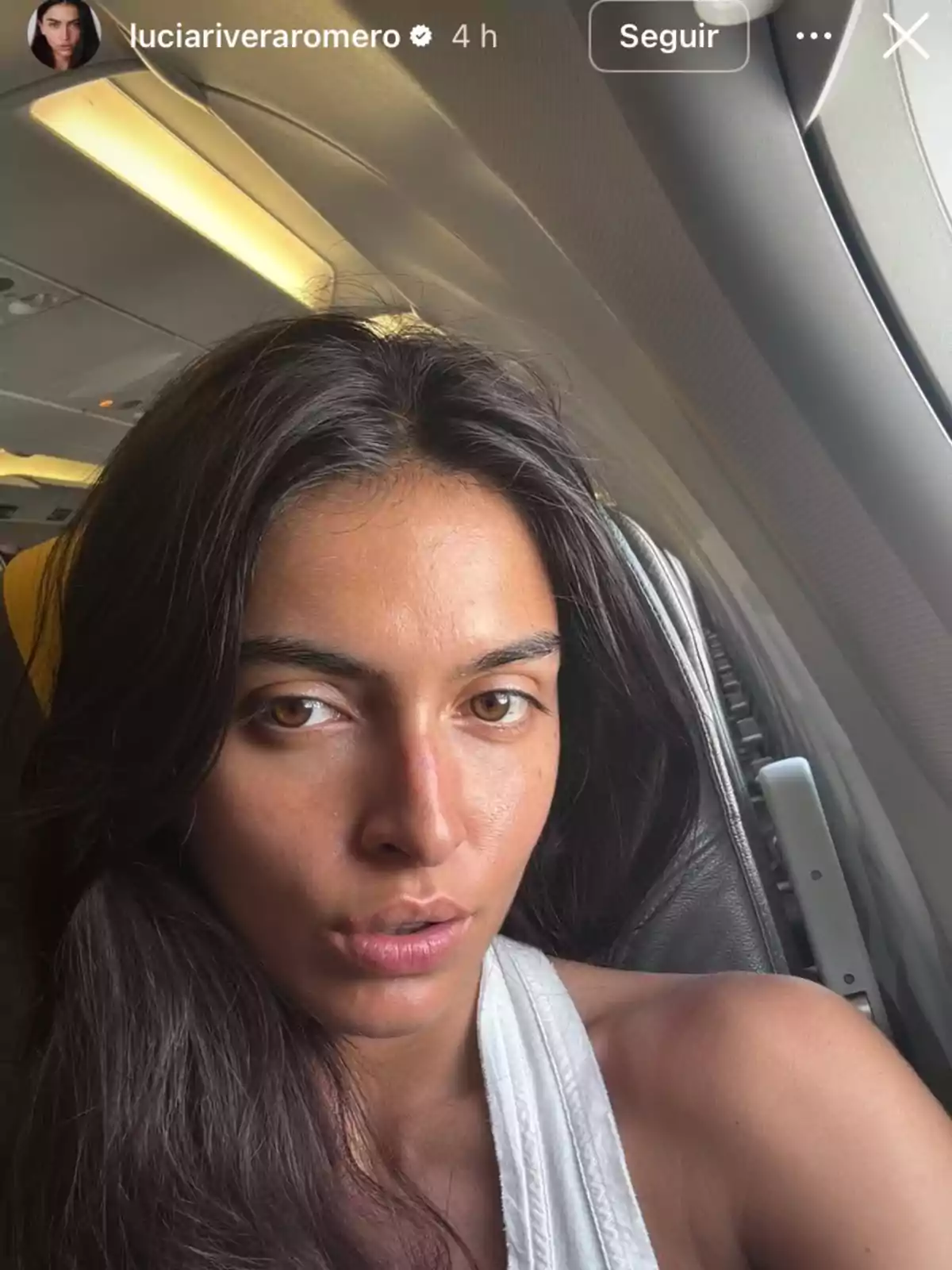 Long-haired, dark-haired woman sitting by an airplane window looking at the camera Long-haired, dark-haired woman sitting by an airplane window looking at the camera