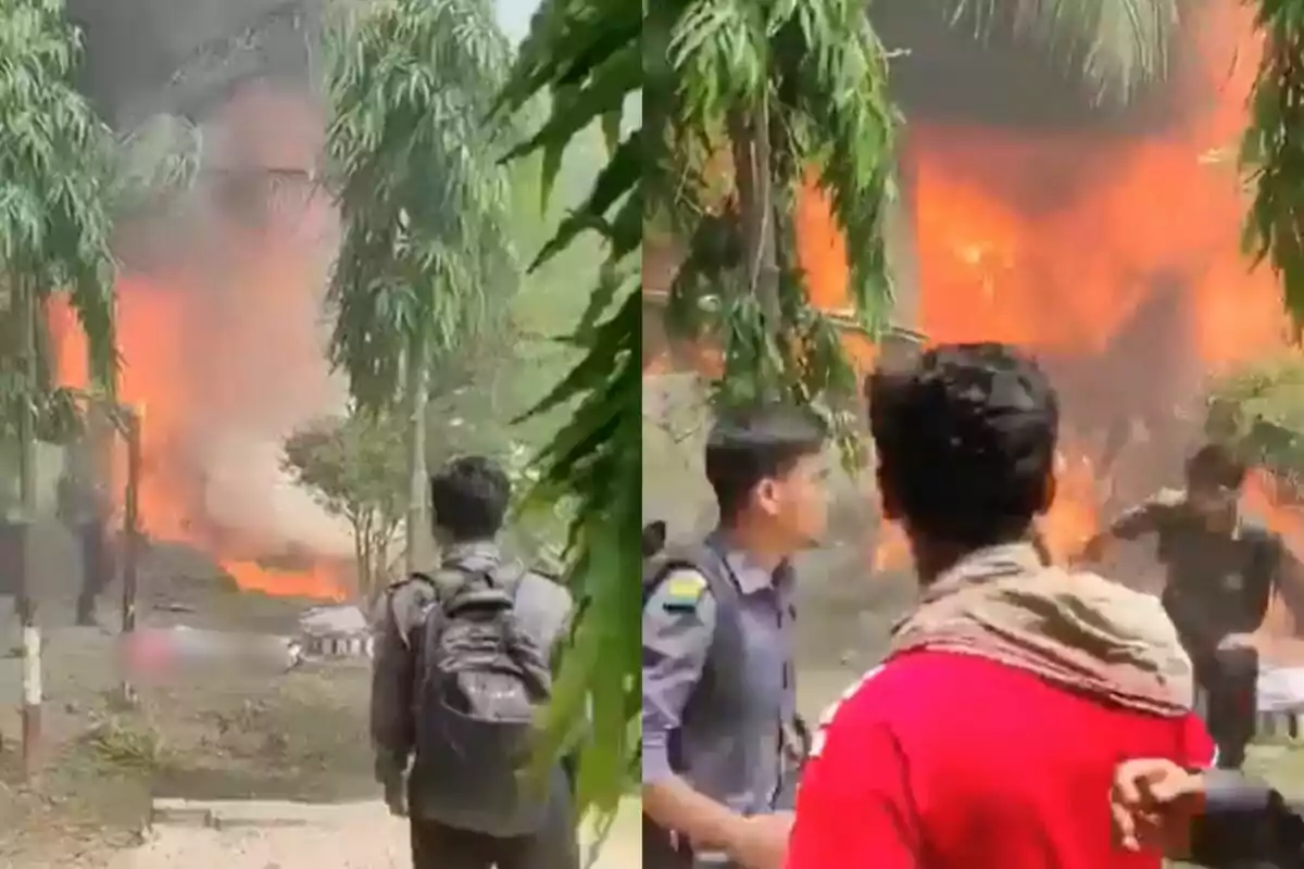 Diverses persones observen un incendi de gran magnitud en una zona arbrada durant el dia, amb flames i fum visibles al fons.