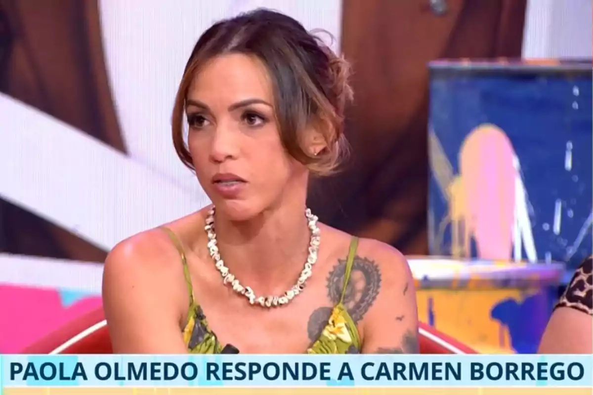 Woman in a green dress and shell necklace sitting on a TV set with a sign that reads Woman in a green dress and shell necklace sitting on a TV set with a sign that reads