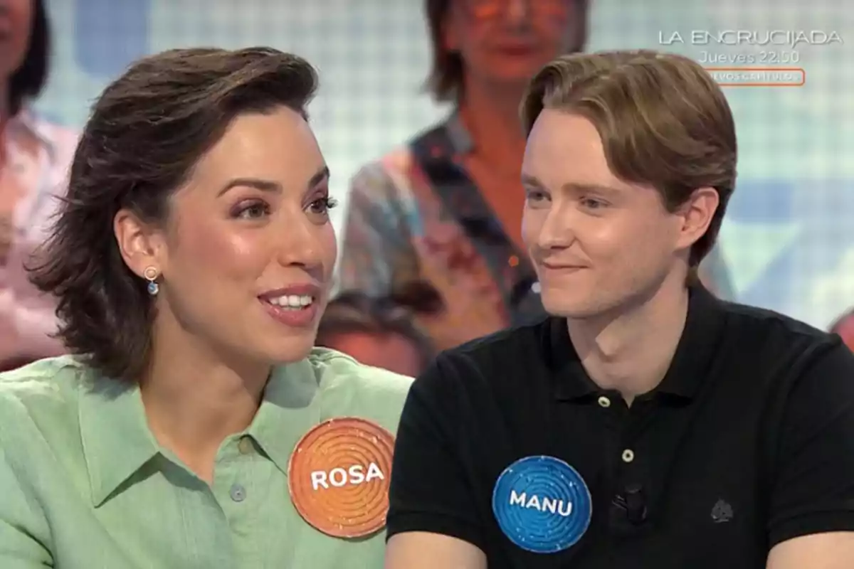 Rosa y Manu sonríen y conversan en un programa de televisión, cada uno lleva una chapa con su nombre, Rosa y Manu, mientras el público observa al fondo. Rosa y Manu sonríen y conversan en un programa de televisión, cada uno lleva una chapa con su nombre, Rosa y Manu, mientras el público observa al fondo.