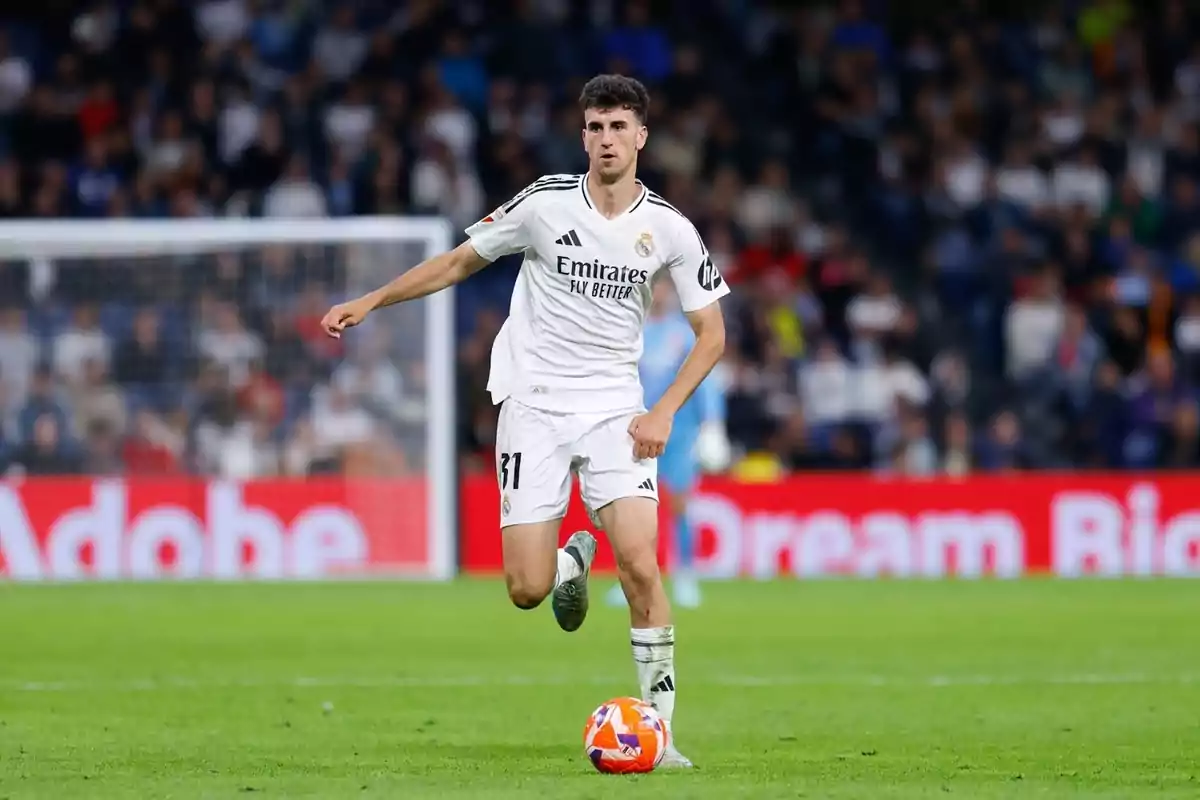 Futbolista del Reial Madrid amb uniforme blanc controlant la pilota durant un partit en un estadi ple d’espectadors Futbolista del Reial Madrid amb uniforme blanc controlant la pilota durant un partit en un estadi ple d’espectadors