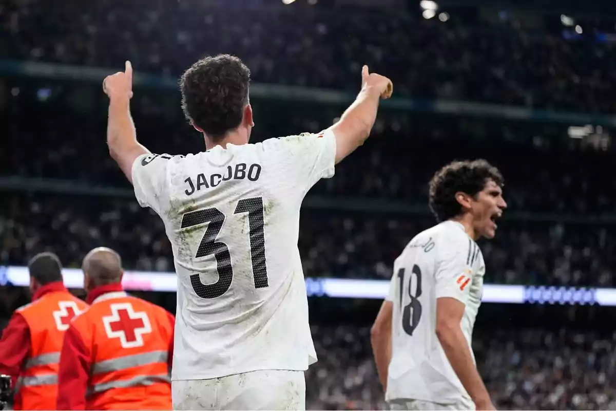 Soccer player wearing number 31 and named Jacobo celebrates with his arms raised while another player shouts excitedly in a stadium full of fans. Soccer player wearing number 31 and named Jacobo celebrates with his arms raised while another player shouts excitedly in a stadium full of fans.