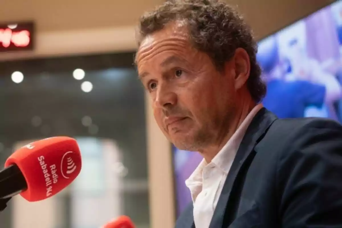 Curly-haired, gray-haired man speaking in front of a red Ràdio Sabadell microphone in a radio studio Curly-haired, gray-haired man speaking in front of a red Ràdio Sabadell microphone in a radio studio