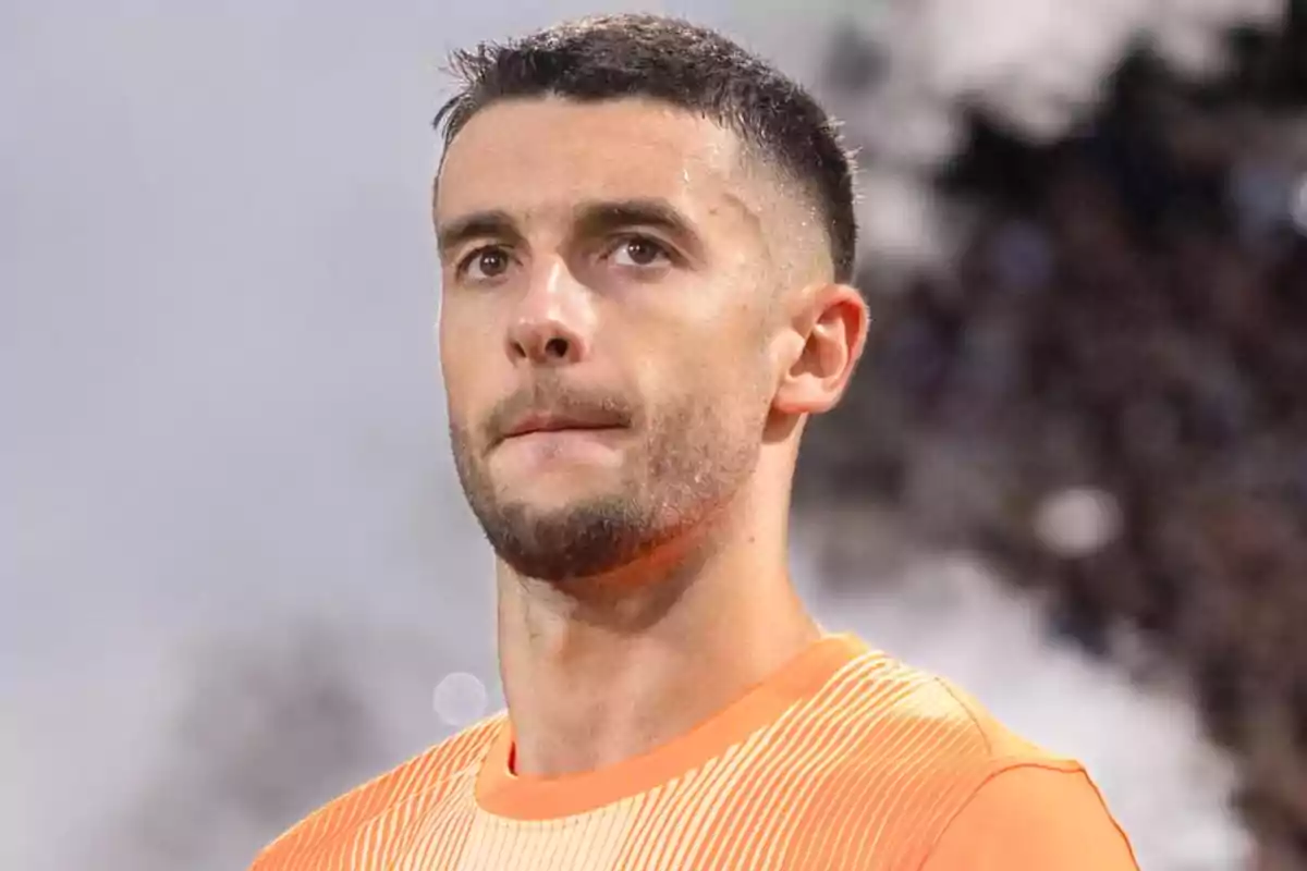 Young man with a short beard and dark hair wearing an orange sports jersey looking straight ahead