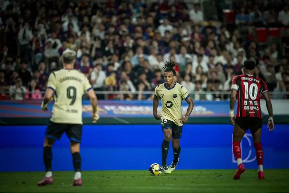 Futbolista del Barcelona avança amb la pilota mentre és observat per un company i un rival en un estadi ple d’espectadors Futbolista del Barcelona avança amb la pilota mentre és observat per un company i un rival en un estadi ple d’espectadors