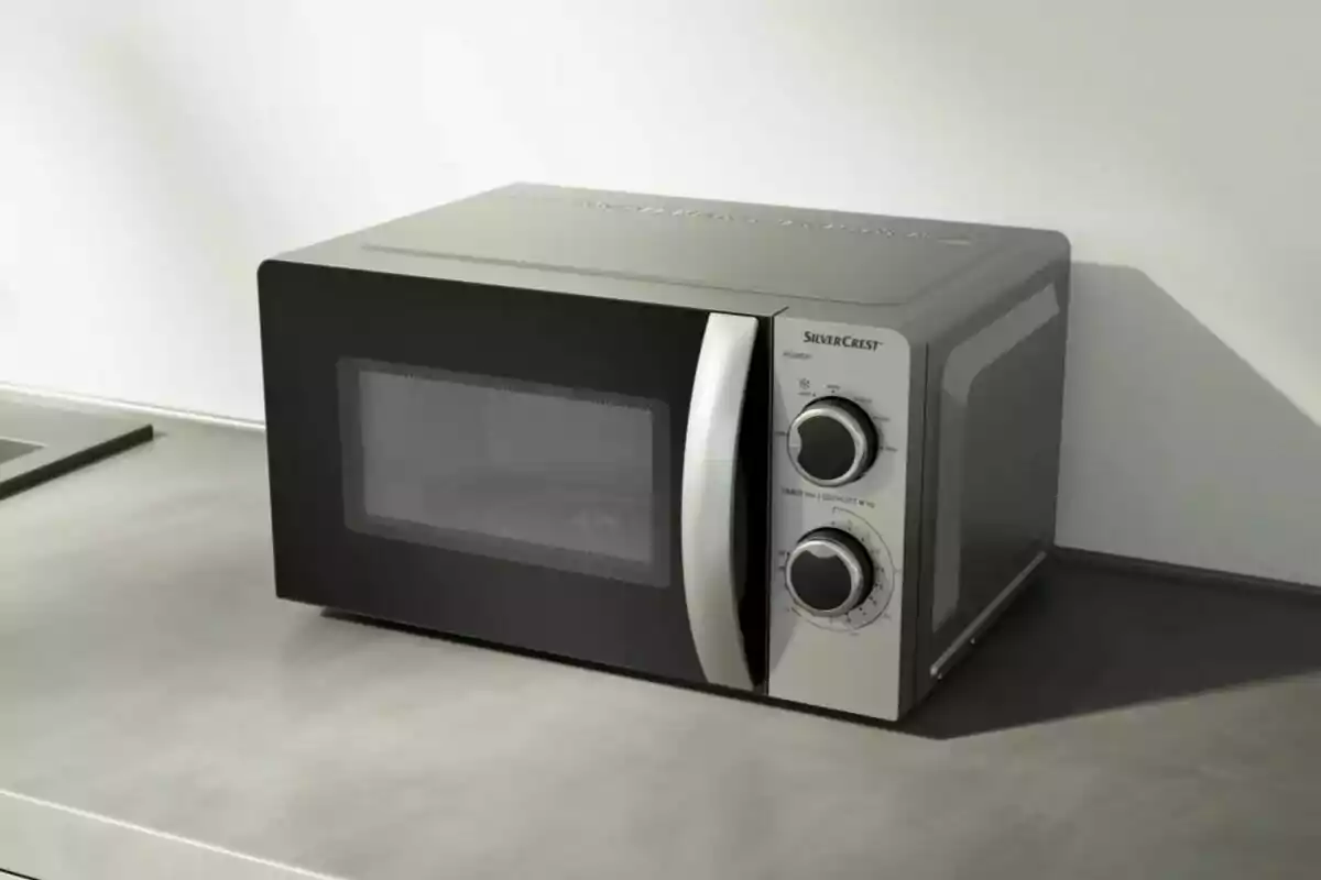 Microondas plateado con puerta negra y dos perillas en una encimera gris Microondas plateado con puerta negra y dos perillas en una encimera gris