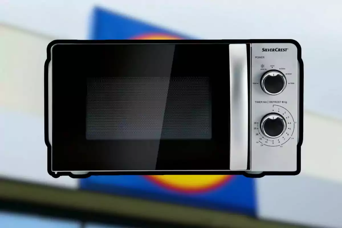 Microondas plateado con puerta negra y dos perillas frontales sobre un fondo desenfocado Microondas plateado con puerta negra y dos perillas frontales sobre un fondo desenfocado