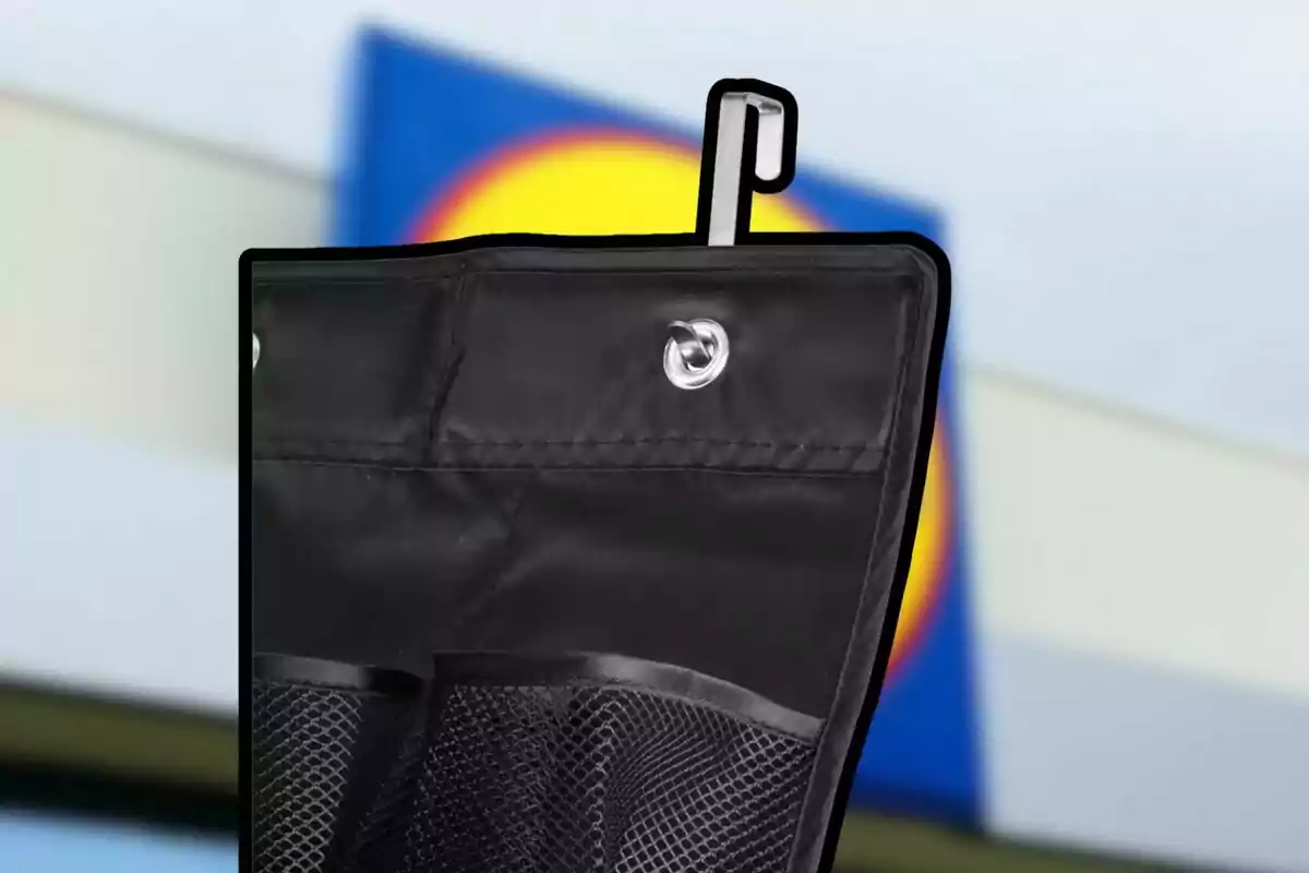 Bolsa organizadora negra con gancho metálico y bolsillos de malla frente a un fondo desenfocado con colores azul y amarillo Bolsa organizadora negra con gancho metálico y bolsillos de malla frente a un fondo desenfocado con colores azul y amarillo