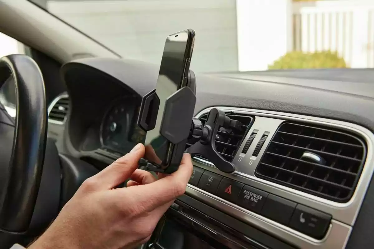 Persona col·locant un telèfon mòbil en un suport per a cotxe subjectat a la reixeta de ventilació del quadre de comandament. Persona col·locant un telèfon mòbil en un suport per a cotxe subjectat a la reixeta de ventilació del quadre de comandament.
