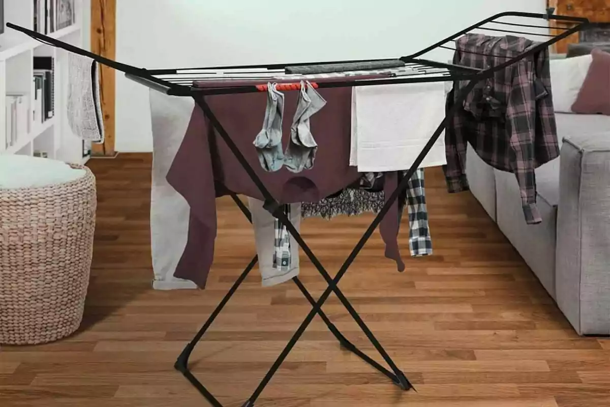 Estenedor de roba negre amb diverses peces penjades en una sala amb terra de fusta Estenedor de roba negre amb diverses peces penjades en una sala amb terra de fusta